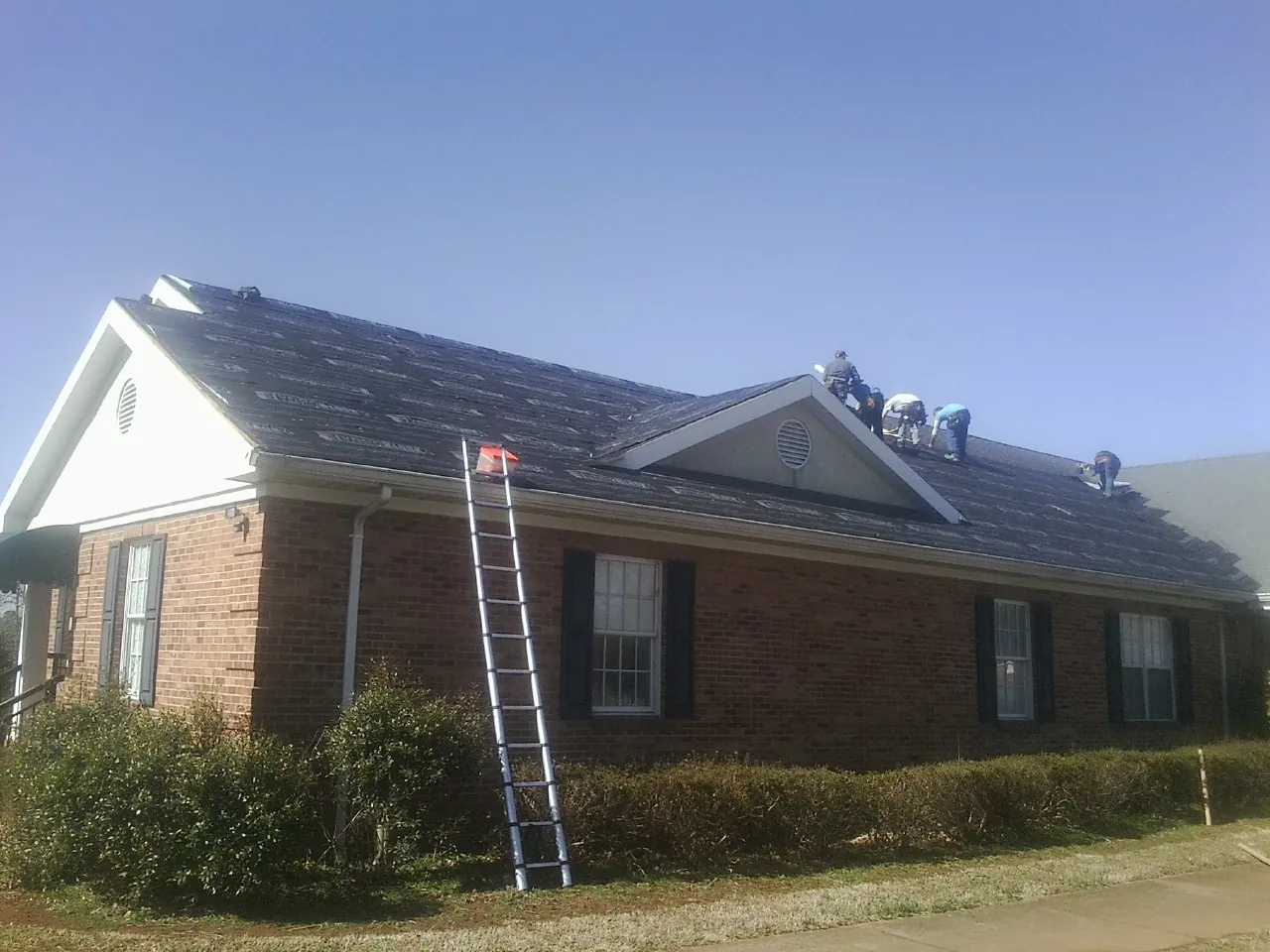 Crew tearing shingles off a brick ranch roof with a ladder set — Emergency Roof Repair work by our crew in Montgomery Creek