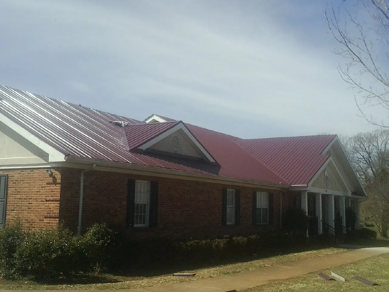 Red metal roof with gabled entries on a long brick building, from a Hail Damage Roof Repair job in Montgomery Creek