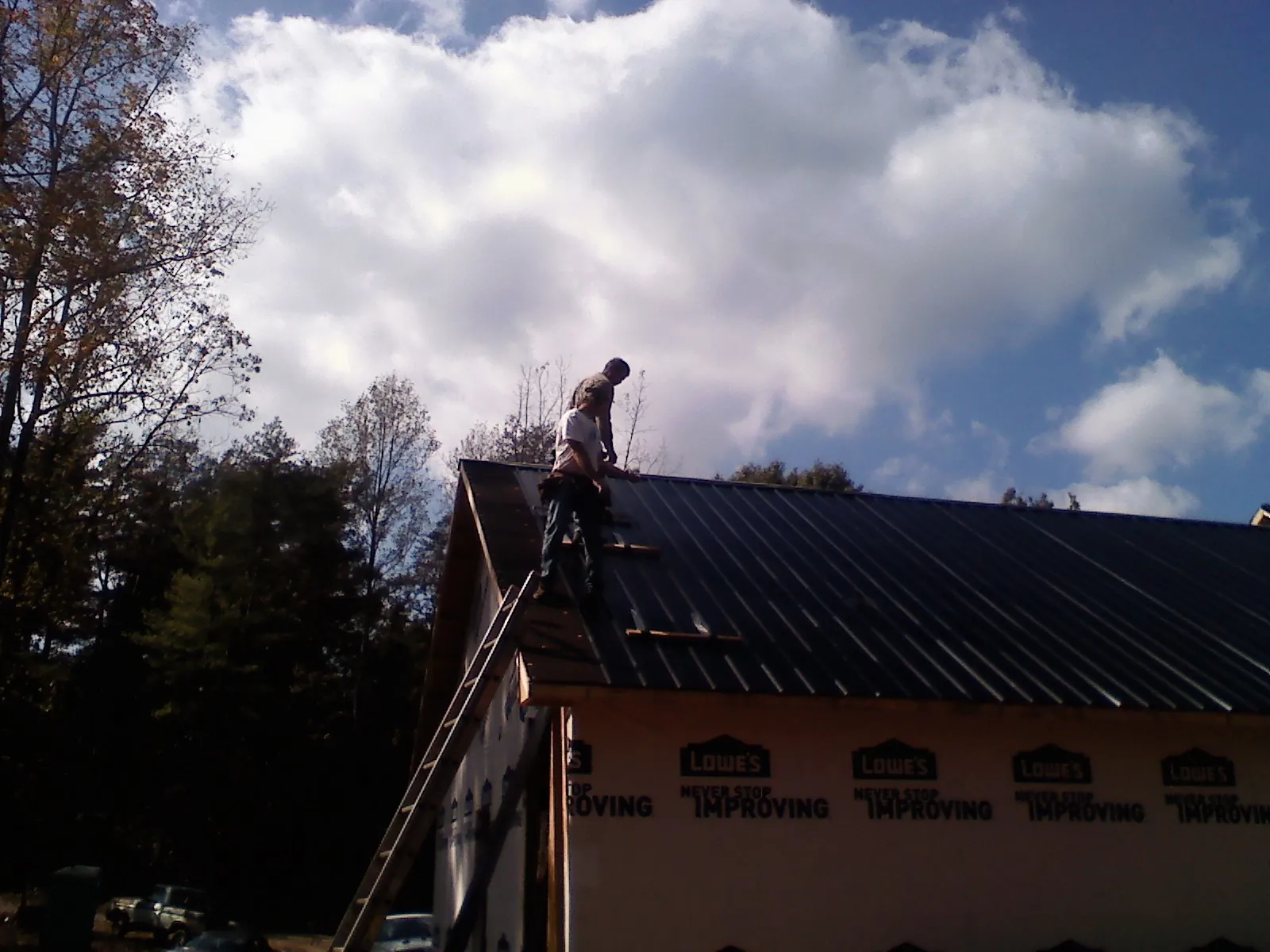 Roofer fastening dark metal panels high against a cloudy sky, from a Roof Inspection job in Montgomery Creek