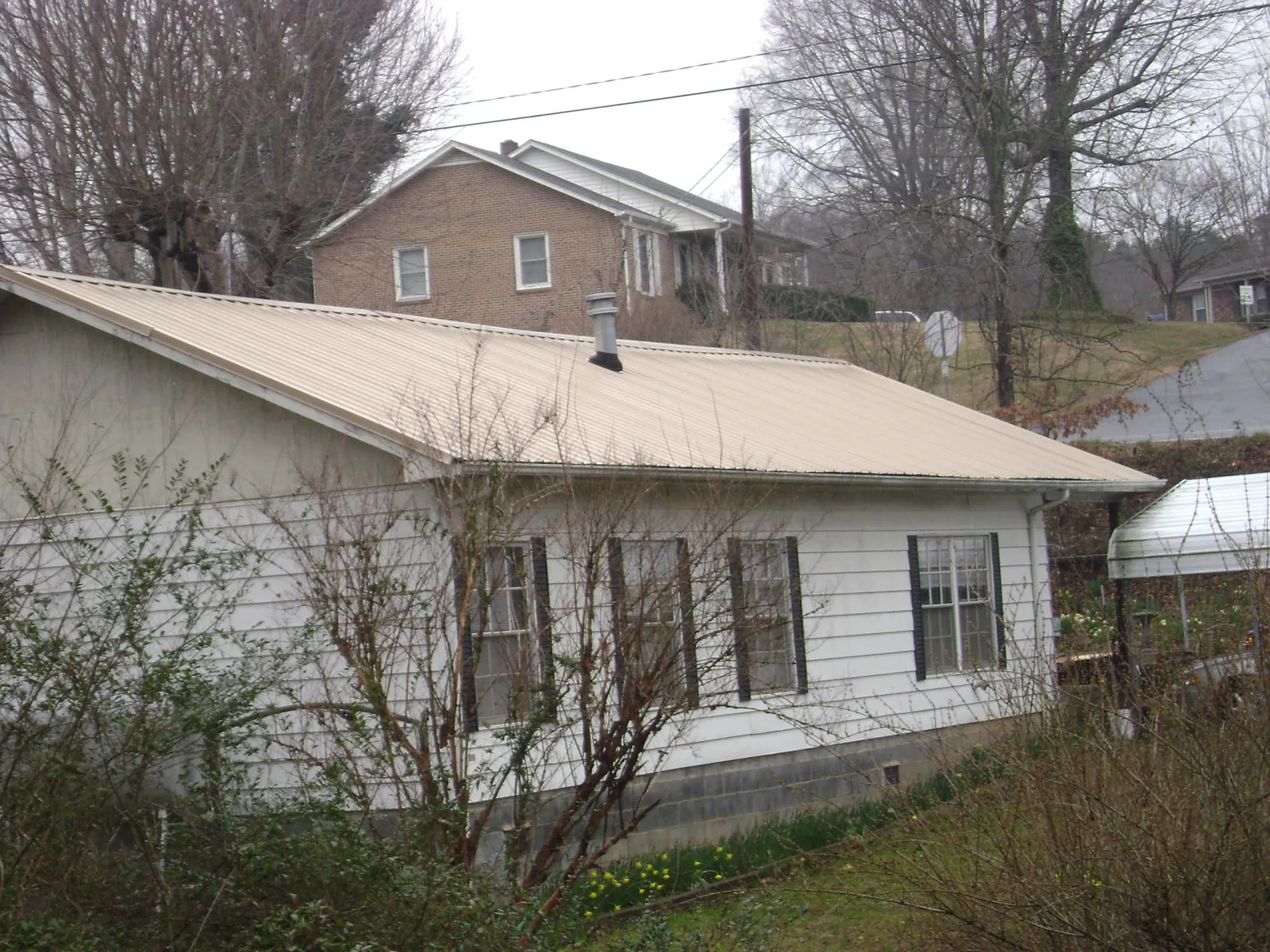 Tan metal roof on a white sided house set into a hillside — Commercial Roofing by Roofing Brothers in Montgomery Creek