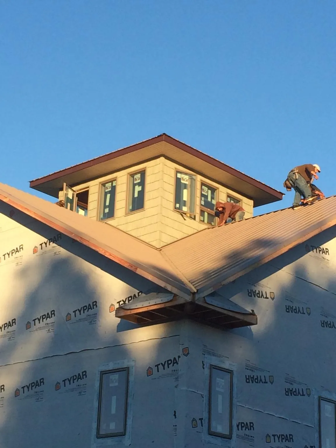 Roofers working around a rooftop cupola on a new metal roof at sunset — Roof Waterproofing in Montgomery Creek by Roofing Brothers